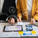 数字机构中两个人的特写镜头，他们正在制定数字营销计划，其中覆盖了设计文档、平板电脑和数字图标。